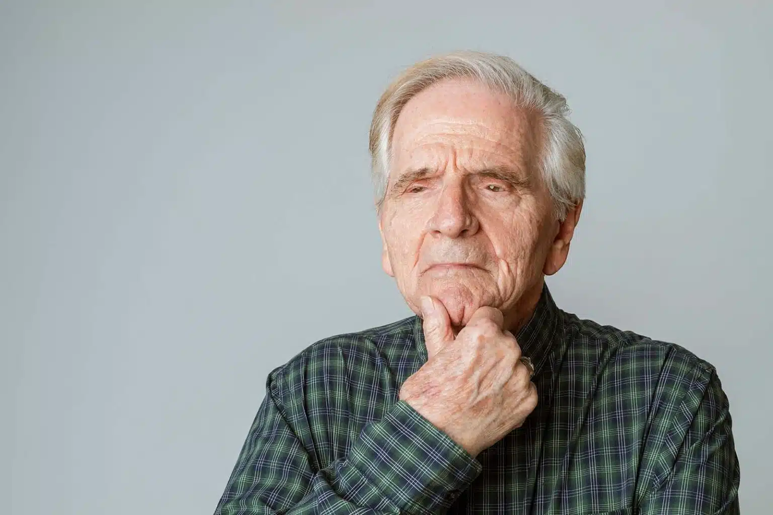 Elderly man with hand on chin looking pensive.
