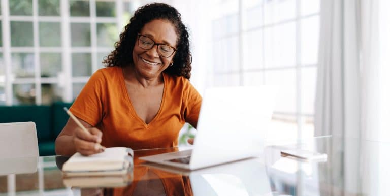 Smiling woman taking notes in front of an open laptop