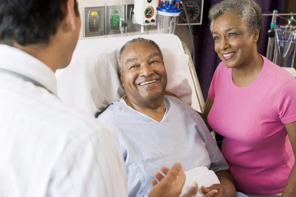 Mature man in hospital bed between his wife and doctor.