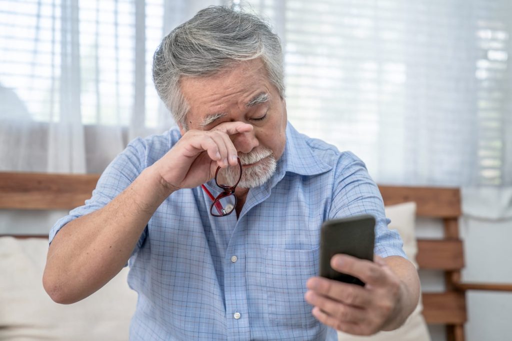 Mature man rubbing eyes while holding phone away from face