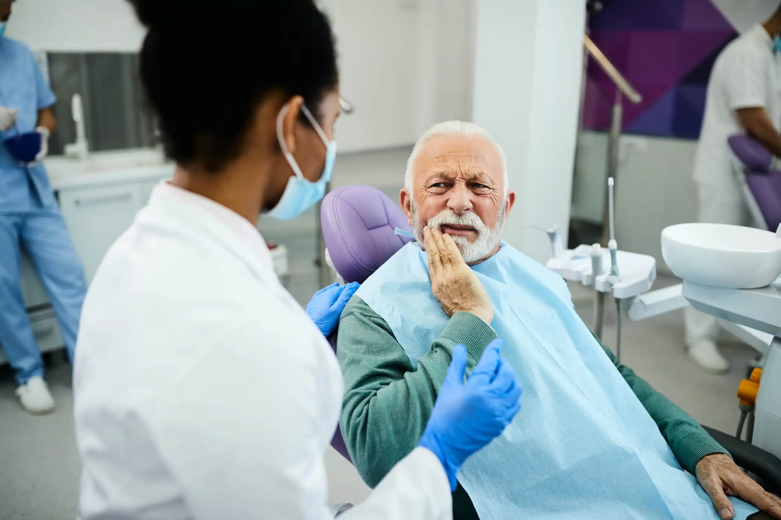 Mature man sitting in dental chair. He is holding his jaw due to a toothache.